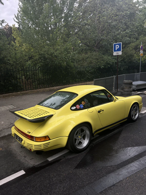Yellow Porsche 911 with a ducktail spoiler parked at the kerb on an overcast street